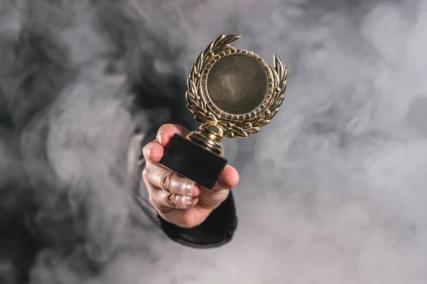 Person is showing a golden medal award trophy through the smoke close up. Winner and first place concept. The champion.