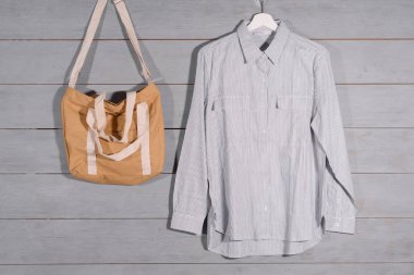 Ahşap duvardaki elbise mağazasında bir çanta ve gömlek askıda asılı..