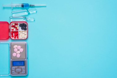 Mavi düz zemin üzerinde çeşitli tıbbi tabletler, şırınga ve dijital ağırlıklar kopya alanı ile yatıyordu.