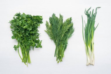 Beyaz düz zemin üzerinde yeşil maydanoz, dereotu ve yeşil soğan dalları uzanır.