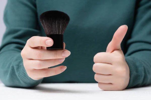 Woman is holding a new makeup brush and is showing a thumbs up gesture. Choosing of make up brush.