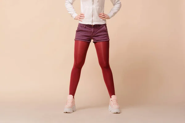 Women in red stockings, sneakers, purple denim shorts on a light background.