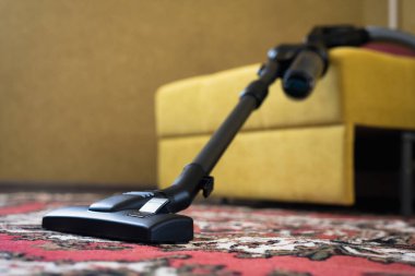 Oturma odasındaki halının üzerinde elektrikli süpürge var..
