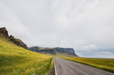 İzlanda 'da yeşil çimenler ve dağların etrafında boş bir yol manzarası. Seyahat ve kartpostal kavramı. İmzalayacak bir yer.