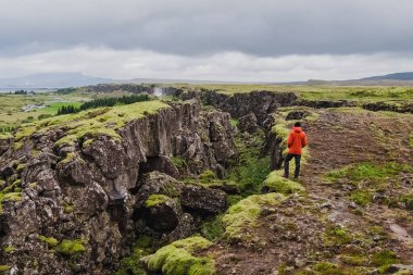İzlanda 'daki Tingvelir Ulusal Parkı' nda kırmızı ceketli bir adam duruyor. Tektonik plaka kırığı. Panoramik fotoğrafçılık