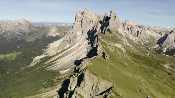 Uma vista deslumbrante do drone para a atração das Dolomitas Monte Seceda. Uma clareira verde com um precipício contra o pano de fundo de rochas gigantes e enormes. e o céu azul. — Vídeo de Stock