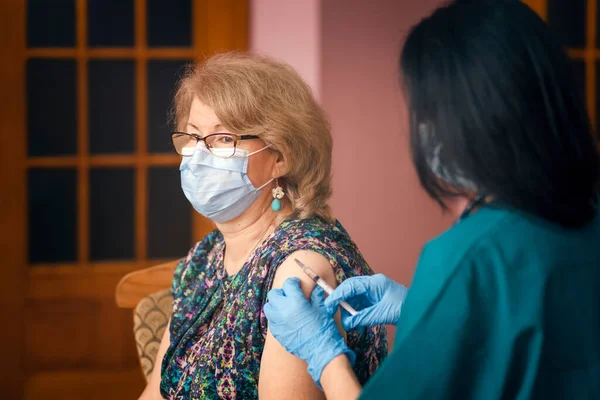 Doktor yaşlı kadına Covid aşısı veriyor.