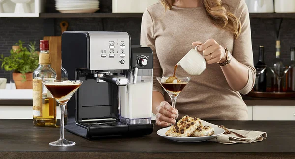 Girl in the kitchen pours coffee into a glass with ice cream, a coffee machine on the kitchen table