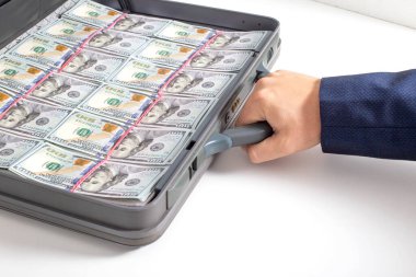 The hand of a man businessman holds a modern briefcase with money dollars on a white background. Fraud and confiscation concept, money agent clipart