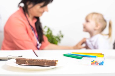 On the table there is a plate with chocolate, in the background the doctor examines a little girl and takes a skin test for food allergies. Establishment of an allergen in children, allergy to sweets clipart