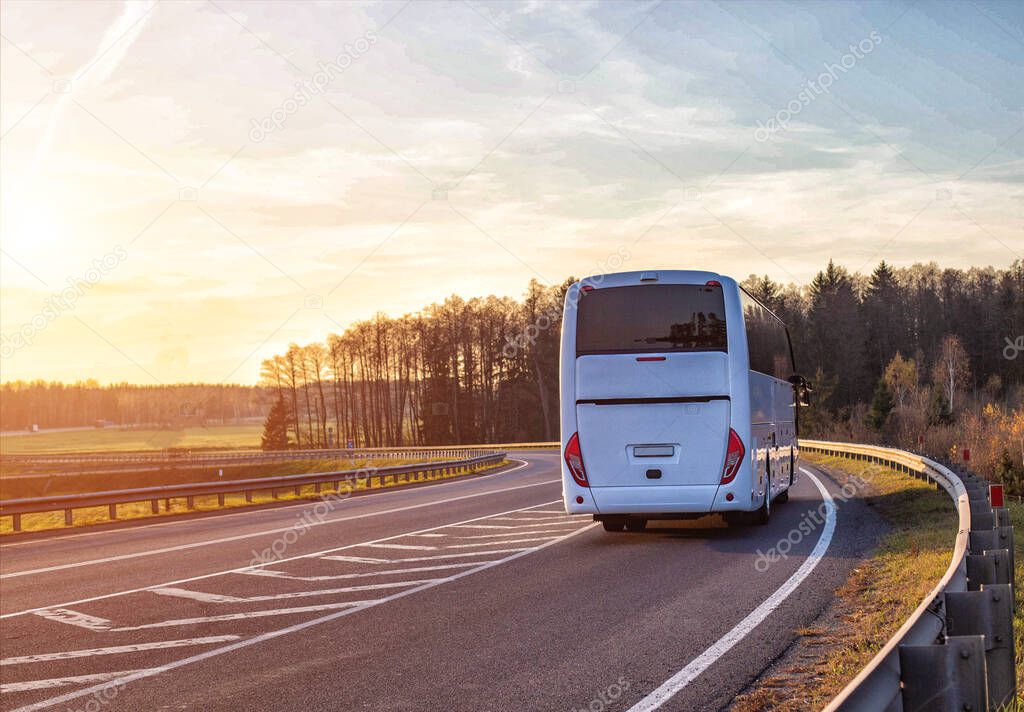 A passenger bus travels along the highway against the backdrop of a forest and a sunset in the sky. Passenger transportation concept, safety and comfort, copy space for text, business