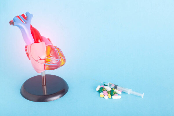 Mock up human heart, pills and syringe on a blue background. Concept of heart disease treatment with medication, pharmacotherapy, copy space for text, antiplatelet drugs