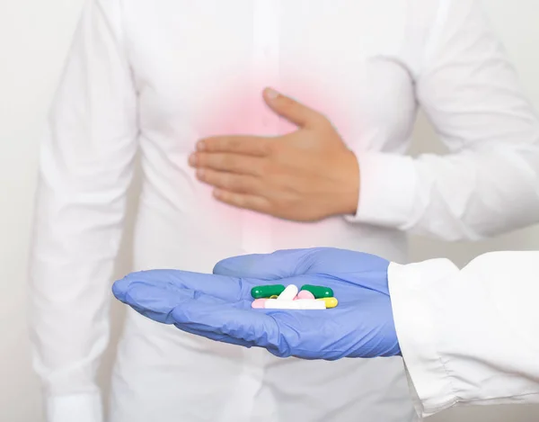 The doctor holds pills in his hand against the background of a man who holds on to the stomach for pain and inflammation in the stomach. The concept of drug treatment of gastritis and stomach ulcers