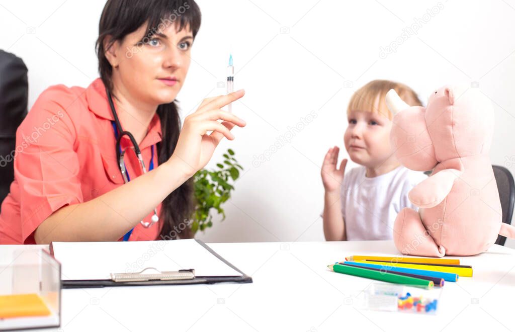 The doctor holds a medical syringe in his hands and a little girl cries nearby in fright. The concept of fear of vaccinations and injections in children, copy space