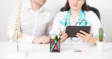 Doktor omurgalı doktor sırt ağrısı olan bir adamın tedavisini ve rehabilitasyonunu tabletine yazıyor. İnsan omurgası modeli, konsültasyon
