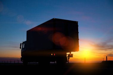 Kamyon şoförü, kargo taşır bir kamyonla, gece gün batımının arka planına karşı. Sürücülerin çalışma ve dinlenme rejimine uyum kavramı, tachograph