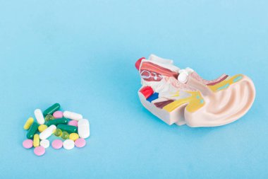 Bir avuç hap ve mavi arka planda kulak taklidi. Uyuşturucu tedavisi, antifungal ilaçlar ve antibiyotiklerle akut otit medya tedavisi kavramı, metin için kopyalama alanı, otomikoz