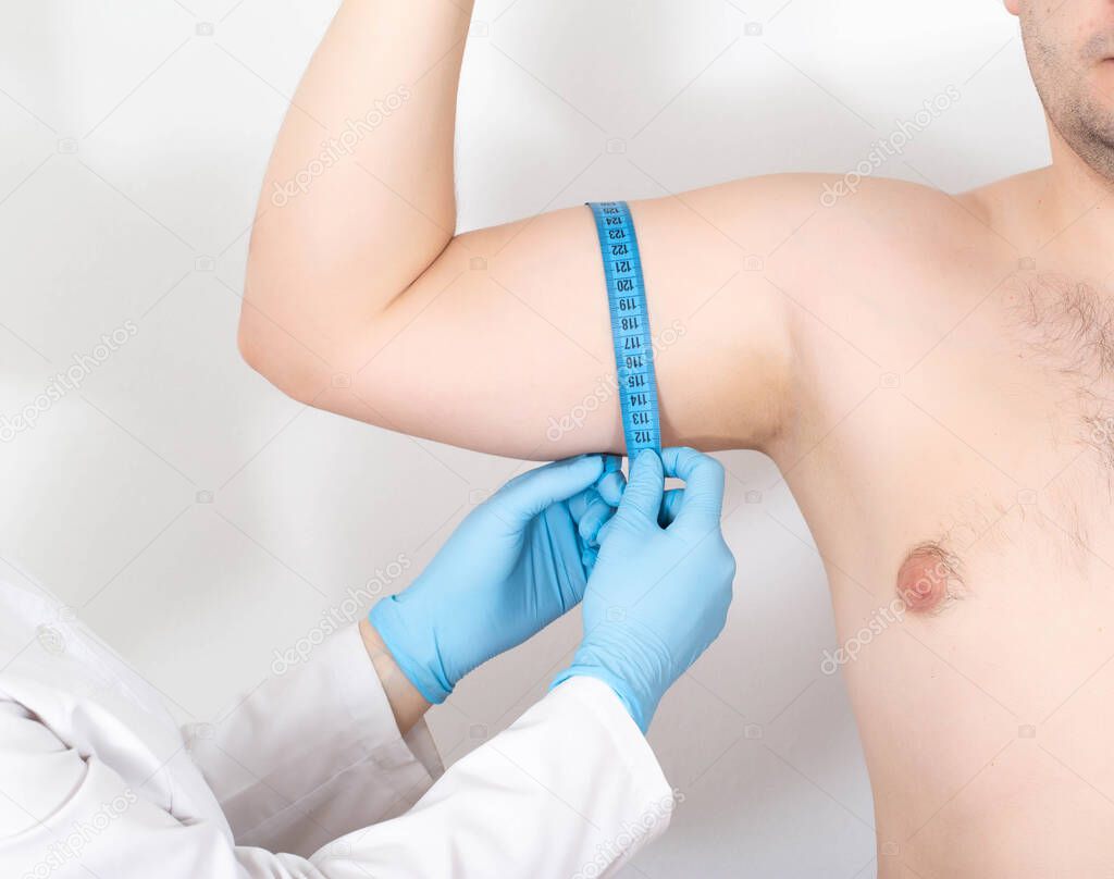 The doctor measures the biceps of a man with a measuring tape to increase the biceps using a surgical operation. Biceps tendonitis
