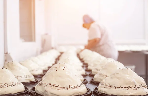 Making sponge cakes with cream at a confectionery factory. Cook decorates cake with cream, sweet dessert, industry