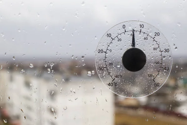 Outdoor outdoor thermometer of air temperature outside the window on which there are raindrops. Concept early spring, cold weather with rain, copy space for text