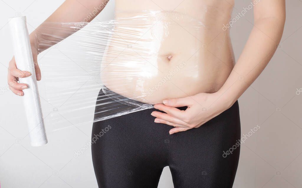 The girl makes an anti-cellulite wrap on her stomach at home. Concept for improving water-salt metabolism in subcutaneous adipose tissue and outflow of fluid