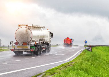 Petrol ürünleri taşımak için kullanılan iki tanker kamyonu yazın yağmur ve bulutlu havada farları açık olarak otoyola çıkıyor. Benzin taşıma konsepti, tehlikeli kargo.