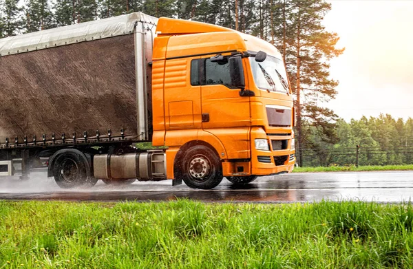 orange modern truck with a semi-trailer is driving on a wet road in the rain. Slippery road, tire grip