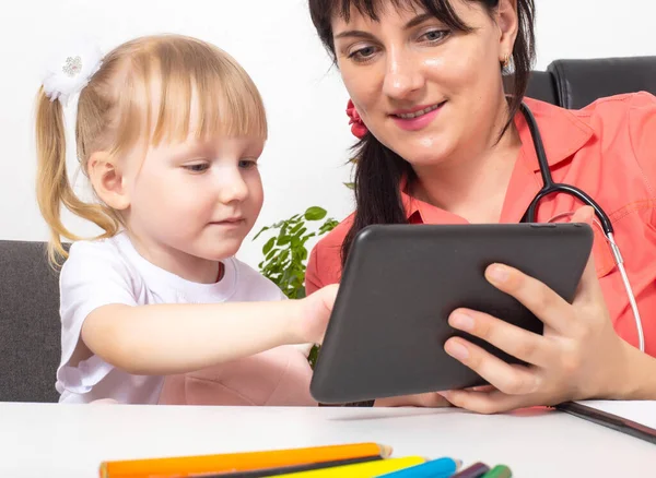 Una doctora, pediatra, muestra una caricatura de una niña de 3-4 años en una tableta. Un enfoque individual para el tratamiento de cada niño. Medicina pediátrica —  Fotos de Stock