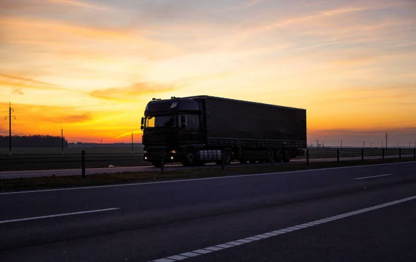 Un camión con semirremolque basculante transporta una carga de grupaje contra el telón de fondo de una puesta de sol nocturna, crepúsculo. El concepto del costo del transporte de mercancías por camiones, la industria. Mercancías —  Fotos de Stock