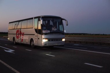 Bobruisk-Minsk Yolu, BELARUS 18.06.19: Farları yanan bir yolcu otobüsü mavi bir akşam gökyüzünün arka planına doğru yol alıyor. Metin ve iş için boşluk kopyala