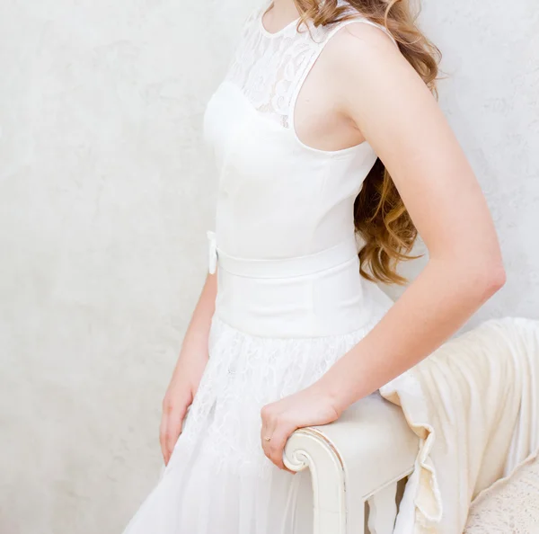 Mujer en un vestido blanco de pie cerca de sofá blanco — Foto de Stock