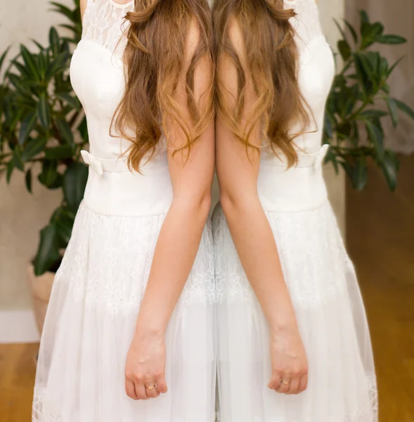Mulher em um vestido branco em pé na frente do espelho — Fotografia de Stock