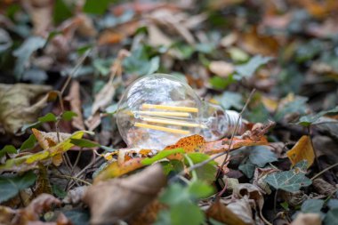 Sarı yaprakların üzerinde bir cep telefonu ve bir ampul var. Ukrayna 'daki savaş yüzünden karartma.