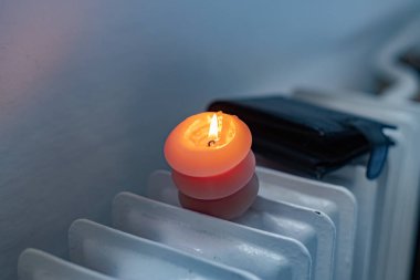 Yanan bir mum, radyatör ve bir cüzdan. Ukrayna 'daki savaş nedeniyle ısıtma fiyatları artıyor.