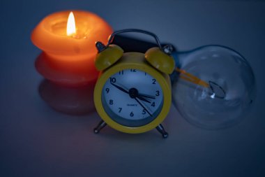 Yanan bir mum, bir ampul ve bir çalar saat. Ukrayna 'daki savaş nedeniyle elektrik kesintileri.