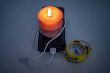 Yanan bir mum, bir güç bankası ve bir çalar saat. Ukrayna 'daki savaş nedeniyle elektrik kesintileri.