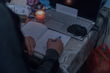 Bir çocuk ödevini mum ışığında çalışmayan bir dizüstü bilgisayarın yanında yapar. Ukrayna 'daki savaş nedeniyle elektrik kesintileri.