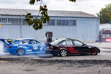 Adrenalin sürüklenme savaşı: asfalt yolda lastik dumanı ile kayan spor arabalar