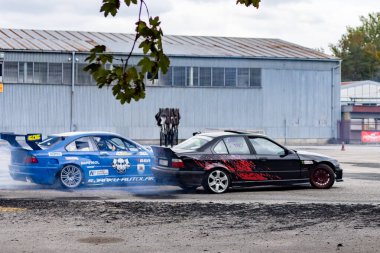 Adrenalin sürüklenme savaşı: asfalt yolda lastik dumanı ile kayan spor arabalar