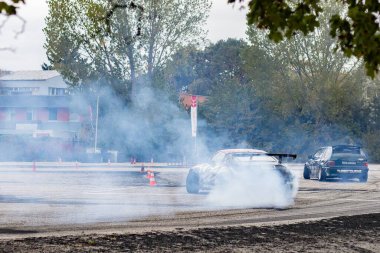 Adrenalin sürüklenme savaşı: asfalt yolda lastik dumanı ile kayan spor arabalar