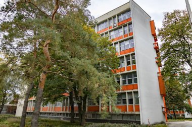 Geometrik balkonları ve yeşil ağaçları olan modernist turuncu ofis binası