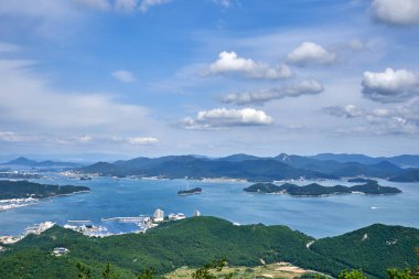 Bereketli yeşil adaların ve Tongyeong, Güney Kore 'nin mavi denizinin huzurlu yüksek açılı manzarası, açık bir yaz gününde dağınık bulutlarla dolu parlak bir gökyüzünün altında..
