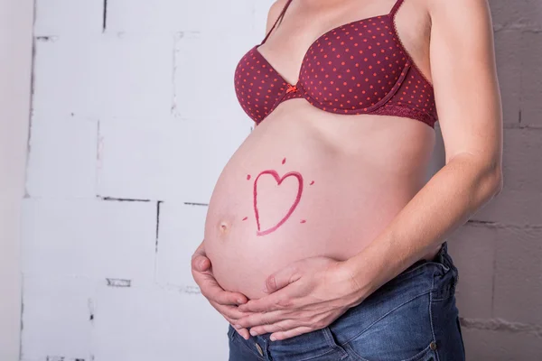 Mulher grávida com símbolo de coração vermelho na barriga — Fotografia de Stock