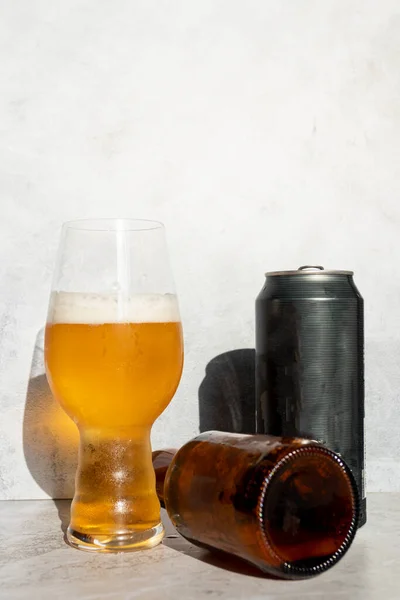 Glass cup served with IPA beer and a bottle and a can at the bottom