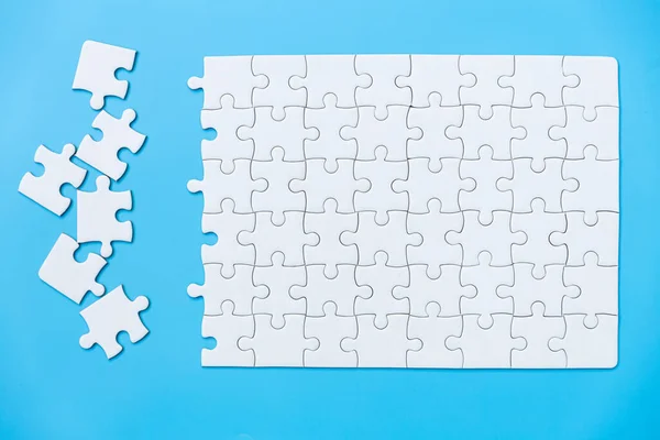 Unfinished white jigsaw puzzle pieces on blue background, The last piece of jigsaw puzzle, Copy space.