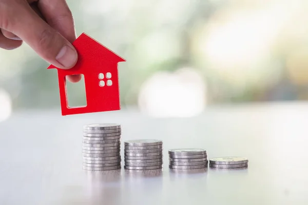 Woman\'s hand putting house model on coins stack. Concept for property ladder, planning savings money of coins to buy a home concept property mortgage and investment for a house.