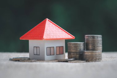 Masada turuncu renkli model evi olan madeni para yığını, finansal strateji fikri. Emlak yatırımı. İpotekler. Kira kontratı. Gelecek ve emeklilik için para biriktir.