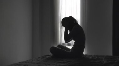 Yalnız genç kadının silueti depresyonda ve stresli hissediyor, karanlık odada el ele tutuşuyor, negatif duygular ve zihinsel sağlık kavramı..