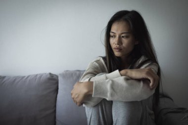 Genç Asyalı kadın evdeki kanepede oturuyor, üzgün, yorgun ve endişeli, akıl sağlığında depresyon geçiriyor. Depresyon, endişe ve uykusuzluk kavramında