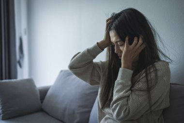Genç Asyalı kadın evdeki kanepede oturuyor, üzgün, yorgun ve endişeli, akıl sağlığında depresyon geçiriyor. Depresyon, endişe ve uykusuzluk kavramında